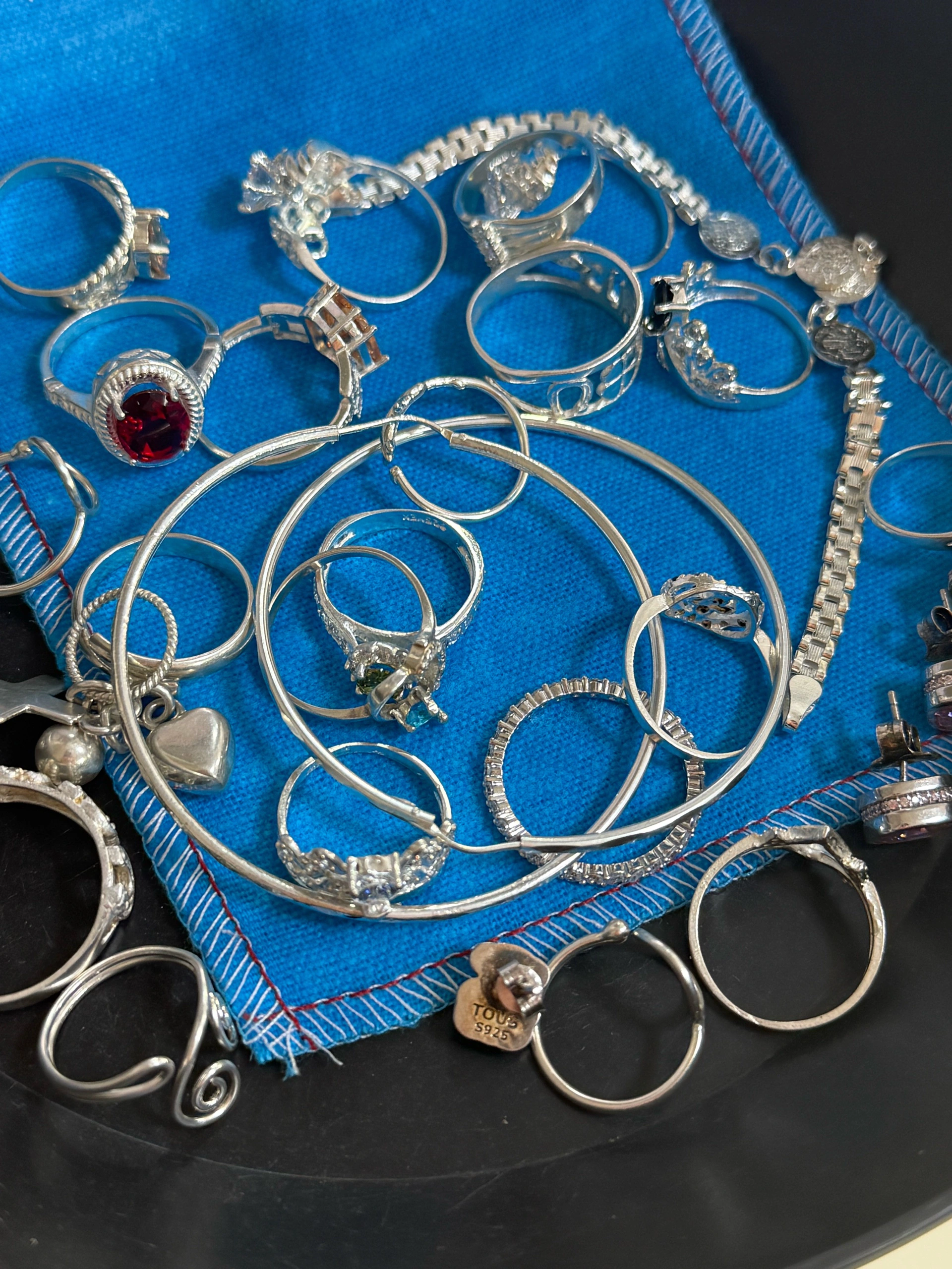 Variedad de anillos y pulseras de plata sobre un paño azul, listos para ser limpiados.